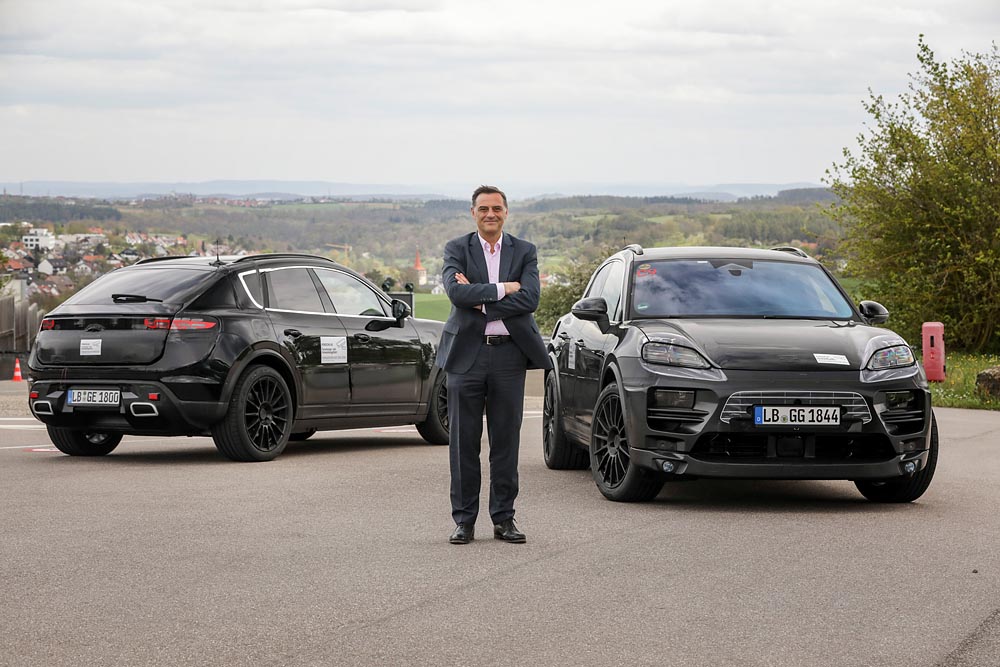 Michael Steiner, Member of the Executive Board, Research and Development, at Porsche AG, in front of two camouflaged prototypes of the all-electric Macan.