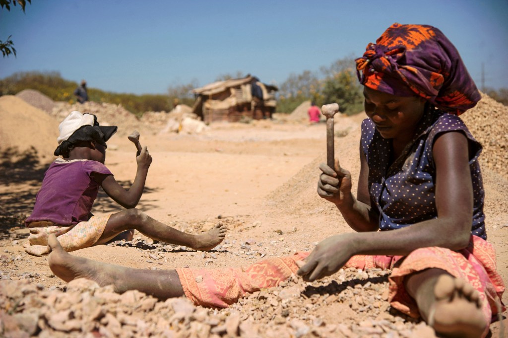 A child and a woman break rocks extracted from a cobalt mine at a copper quarry and cobalt pit in Lubumbashi on May 23, 2016. - The price of copper has fallen heavily, directly impacting workers in the town. (Photo by JUNIOR KANNAH / AFP) (Photo by JUNIOR KANNAH/AFP via Getty Images)