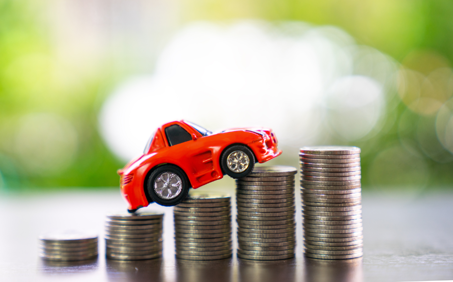 A model car driving up stacks of coins, illustrating rising car insurance costs