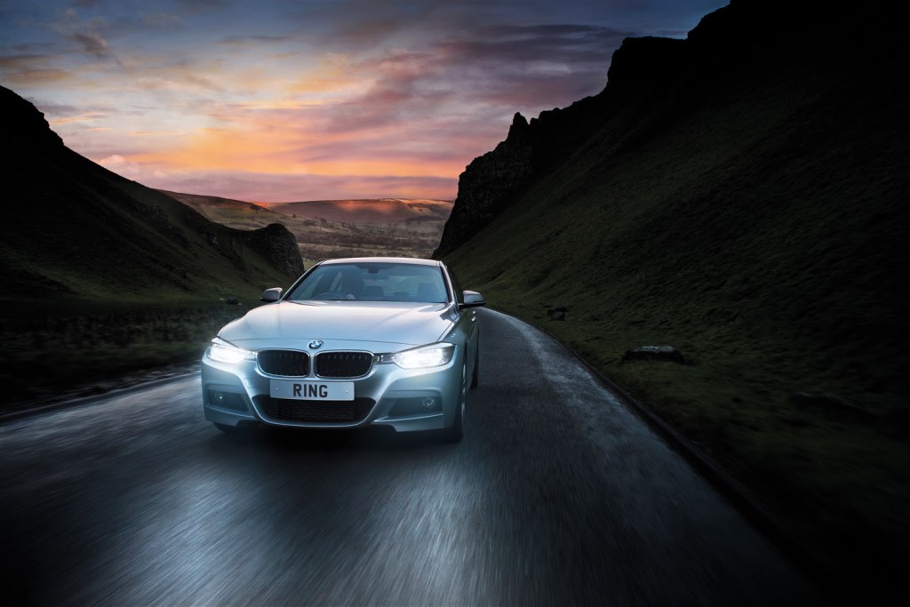 A BMW driving along a hilly road at dusk with the headlights on.