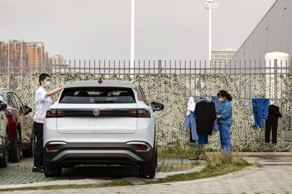 An employee checks on her laundry next to a newly built Volkswagen AG electric vehicle at the automaker's factory, operated with local partner SAIC Motor Corp., in Shanghai, China, on Tuesday, June 7, 2022. Volkswagen AG plans to keep workers at their Shanghai factories isolated in so-called closed loop management systems until June 10, according to people familiar with the matter, even as authorities allow most residents to move freely around the city amid falling Covid-19 cases. Photographer: Qilai Shen/Bloomberg via Getty Images